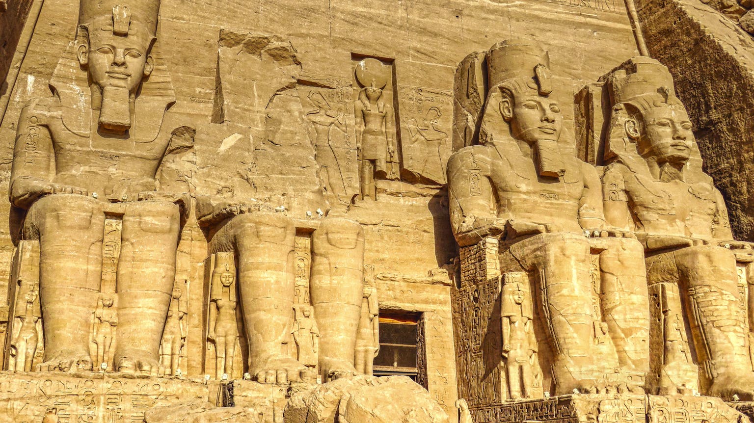 Sculptures of ancient Egyptian Pharaoh carved out of rock with decorative elements representing faces and clothes in sanctuary in Egypt